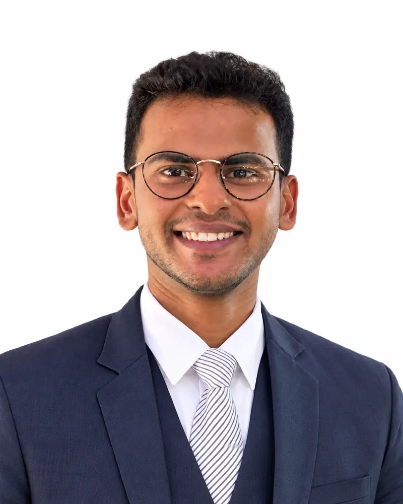 Portrait of Faraz Ansari smiling, in round glasses, a navy three-piece suit and a striped tie